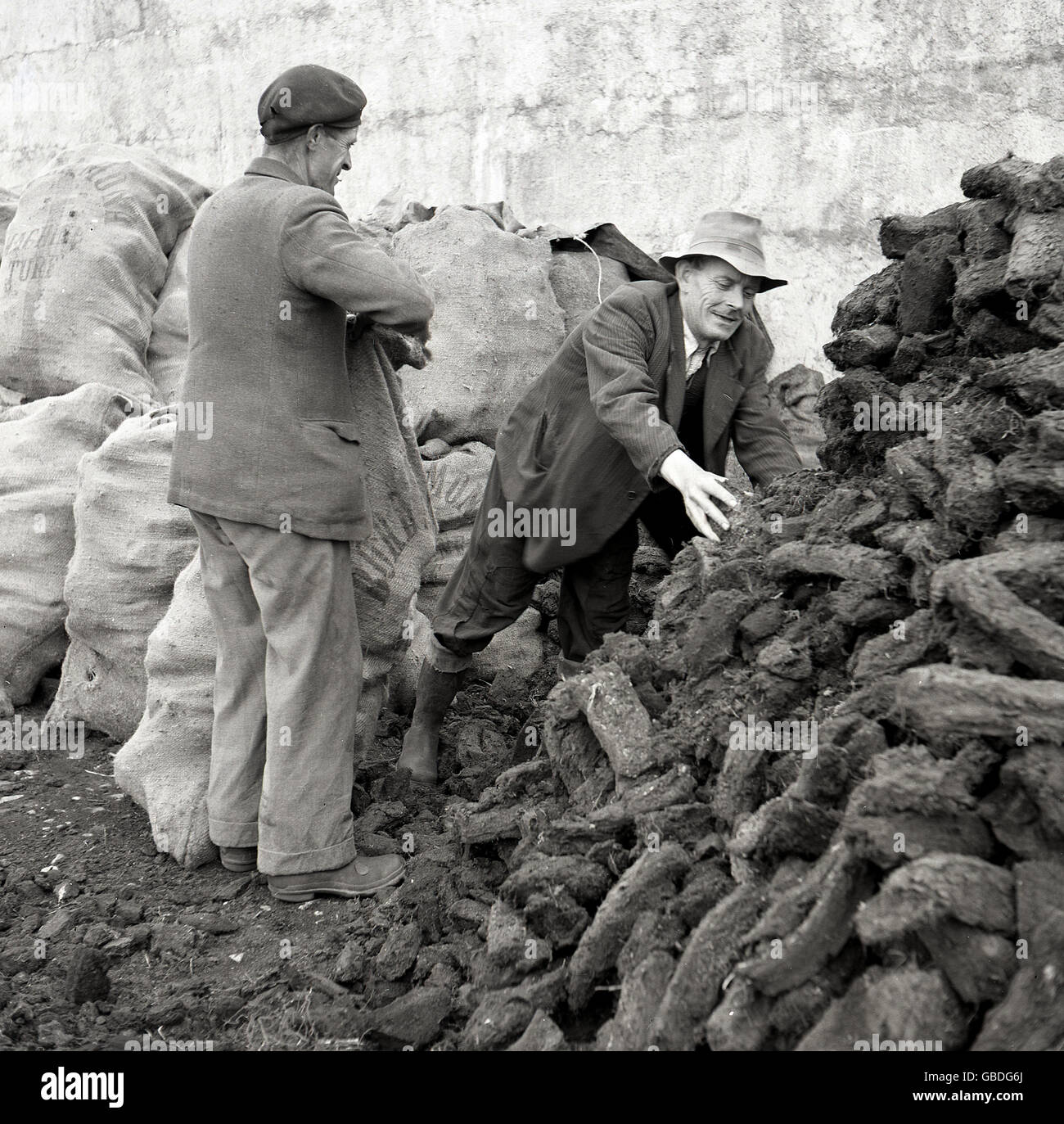 1950s, historical picture of two Irish men putting logs of compressed, dried peat into sacks