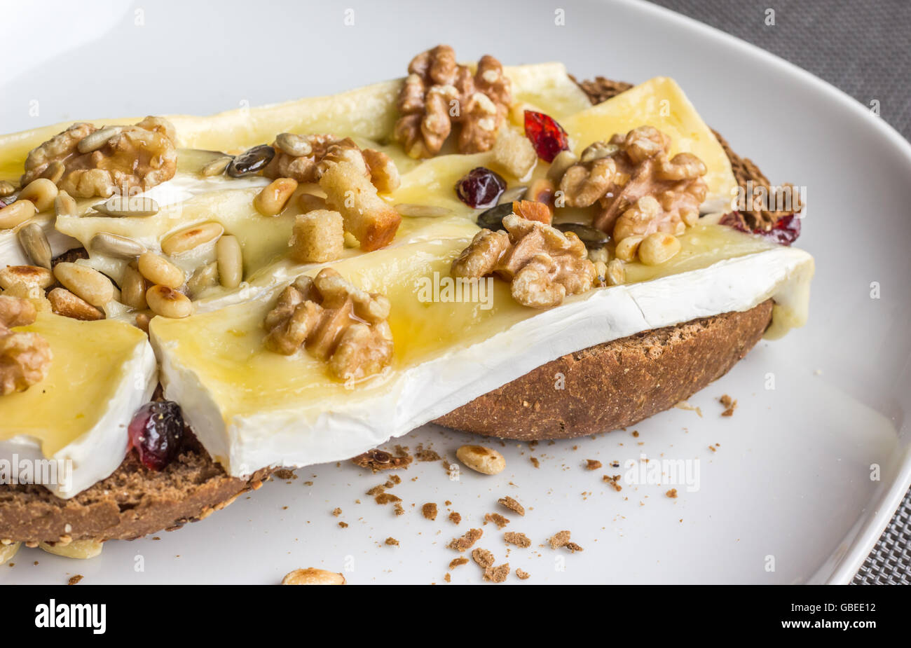 Melted brie with honey, pine nuts and walnuts on dark bread Stock Photo