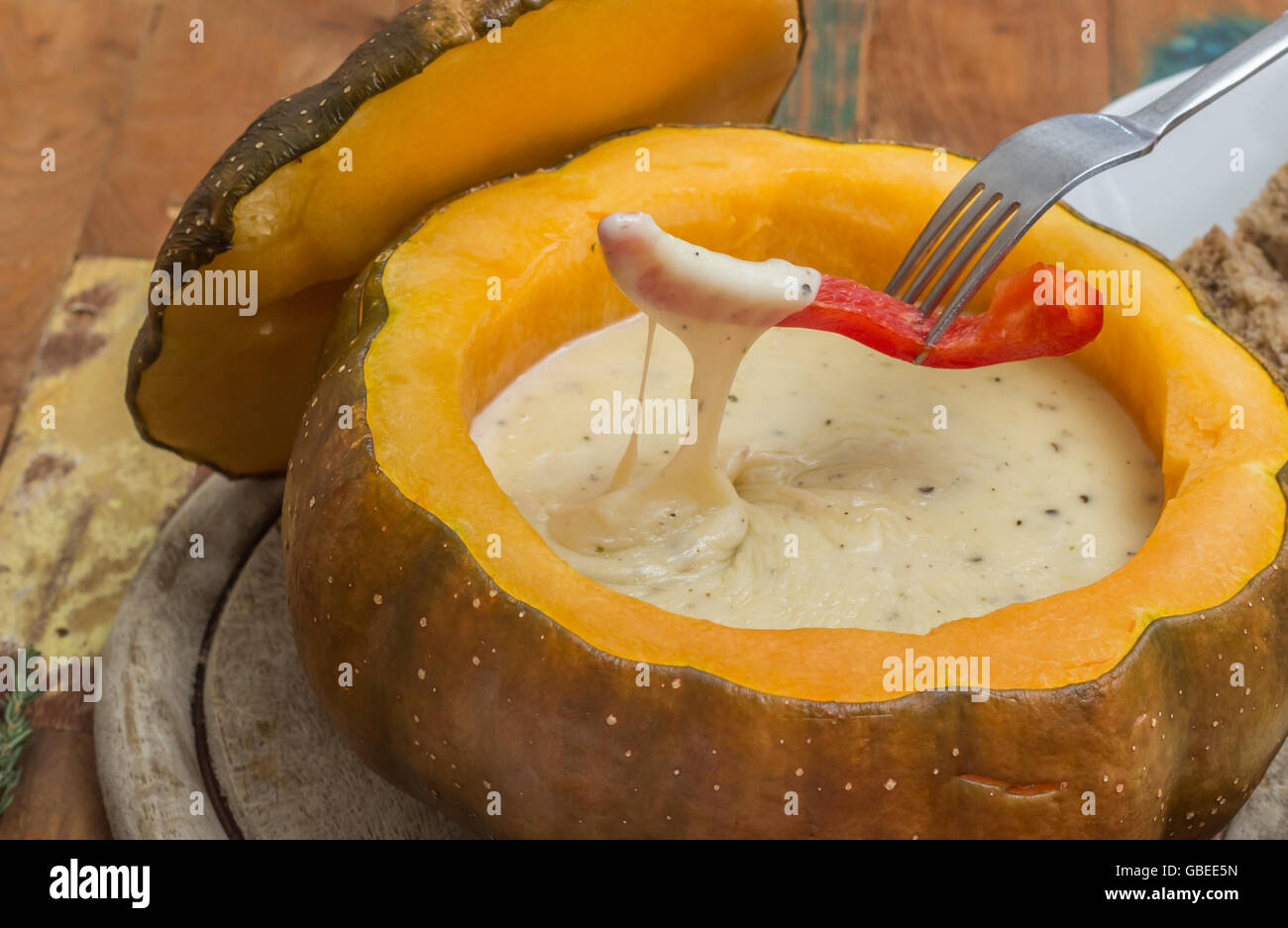 Cheese fondue in a roasted pumpkin with a slice of bell pepper on a