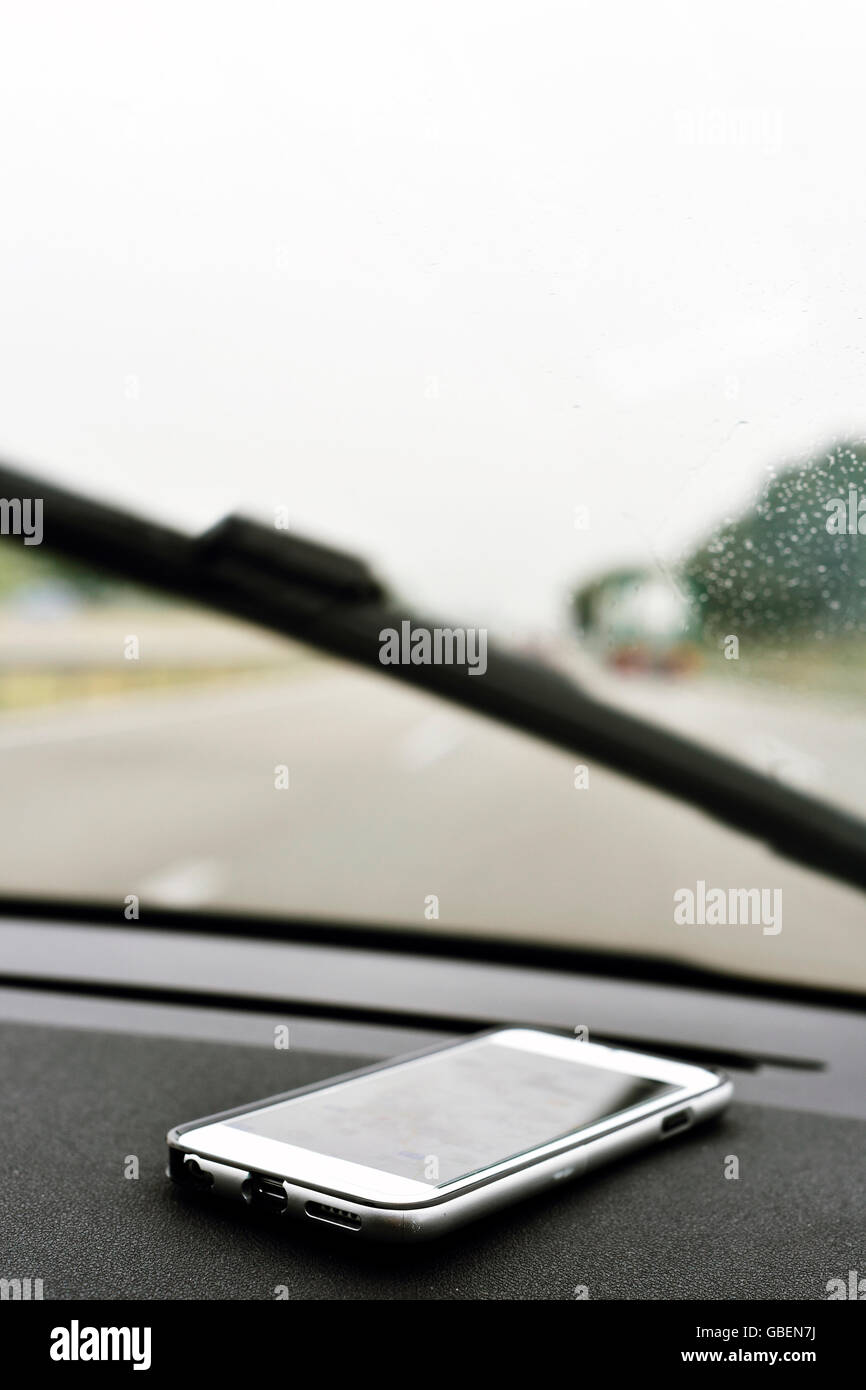 closeup of a smartphone on the dashboard of a car in motion in a road with several lanes, in a rainy day Stock Photo