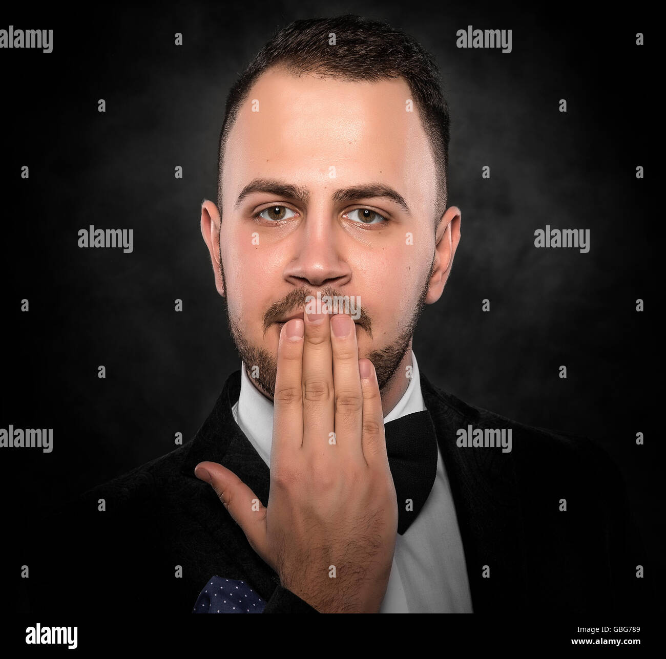 Funny man in suit hand covering mouth over dark background. Stock Photo