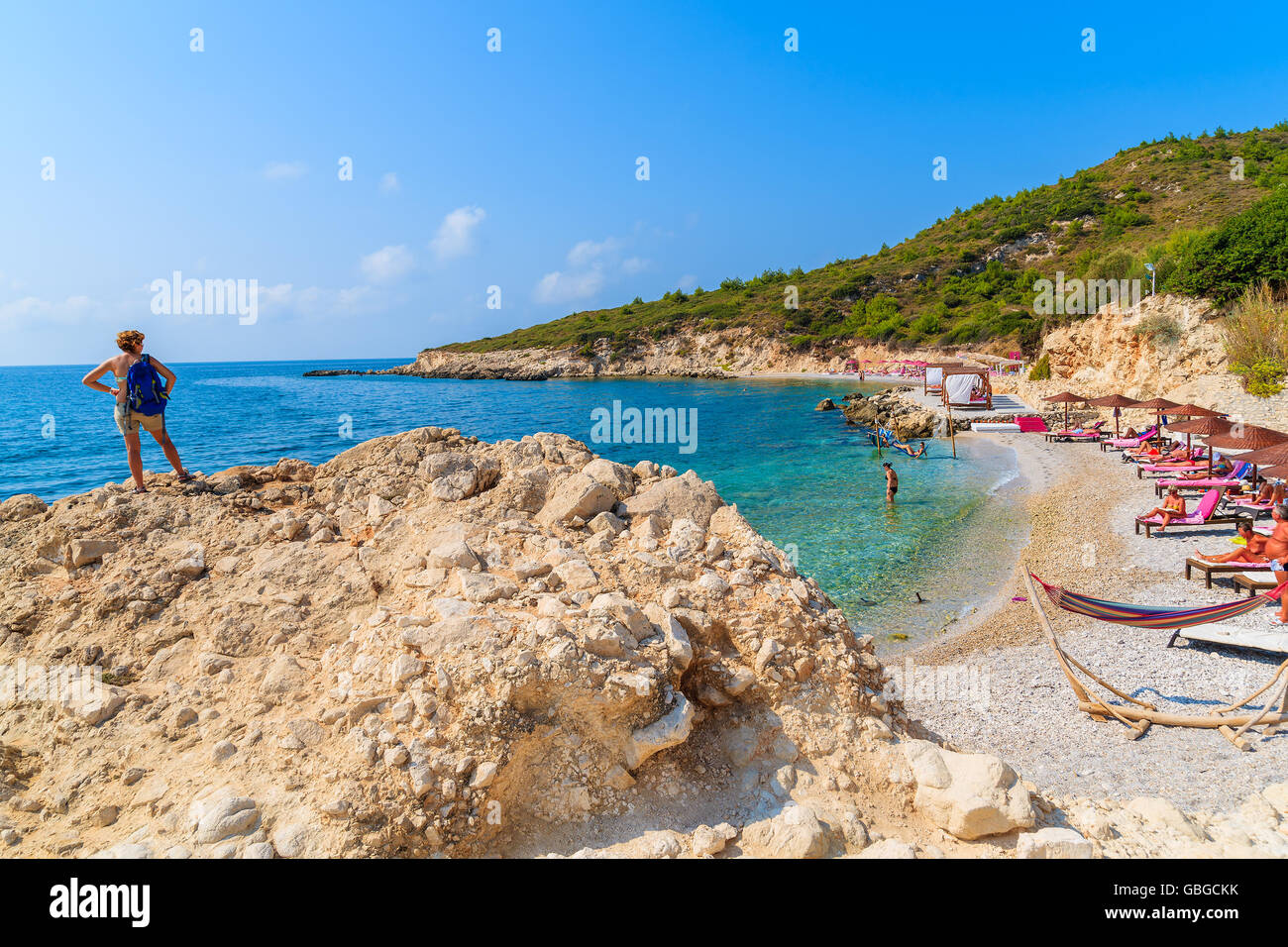 A young woman tourist standing on a rock and looking at beautiful beach in Proteas bay, Samos island, Greece Stock Photo