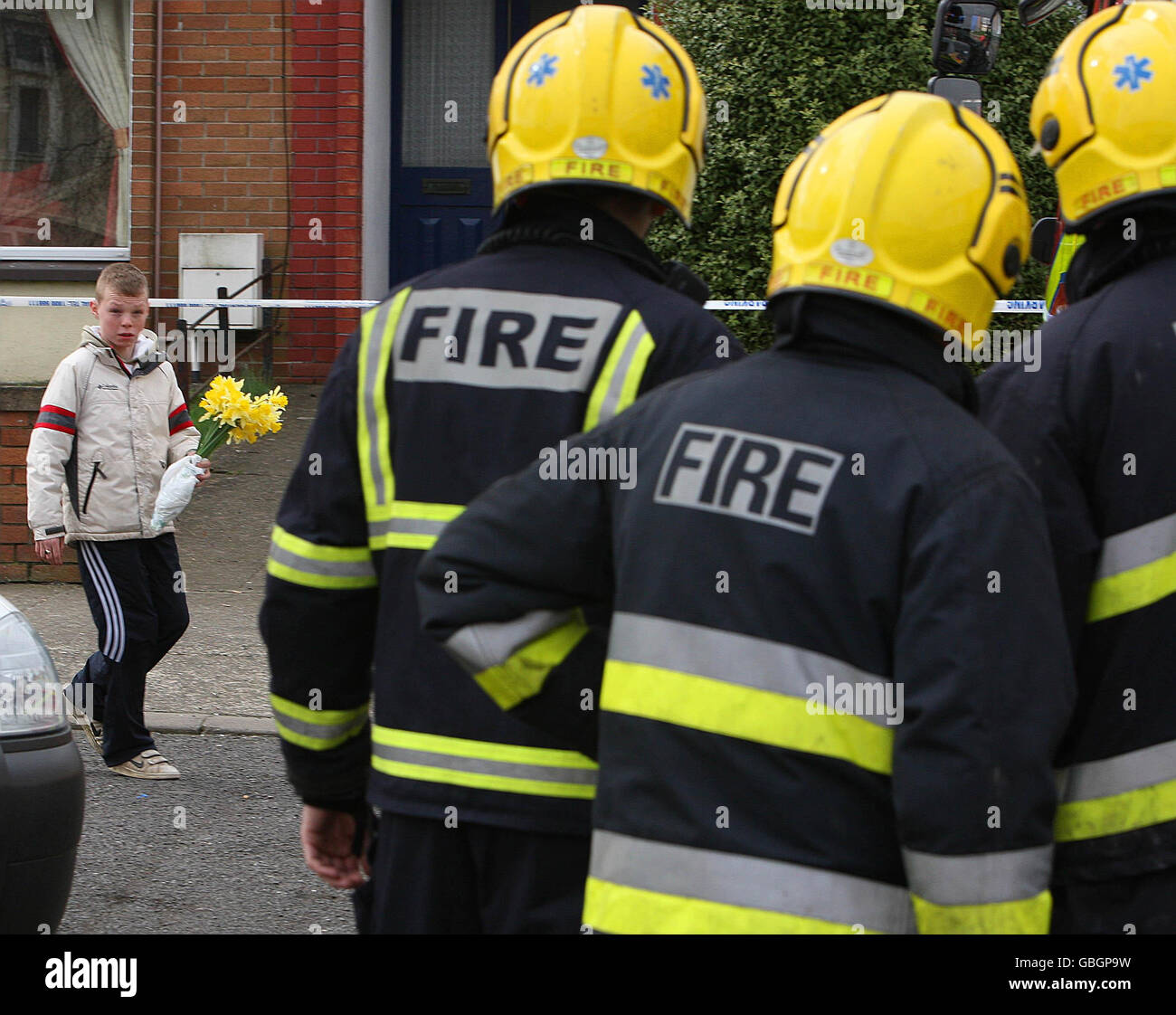 A young boy carries flowers as firefighters, wait at the scene of a house fire on the Moneymore estate in Drogheda, Co Louth, Ireland, where three members of one family died. Stock Photo