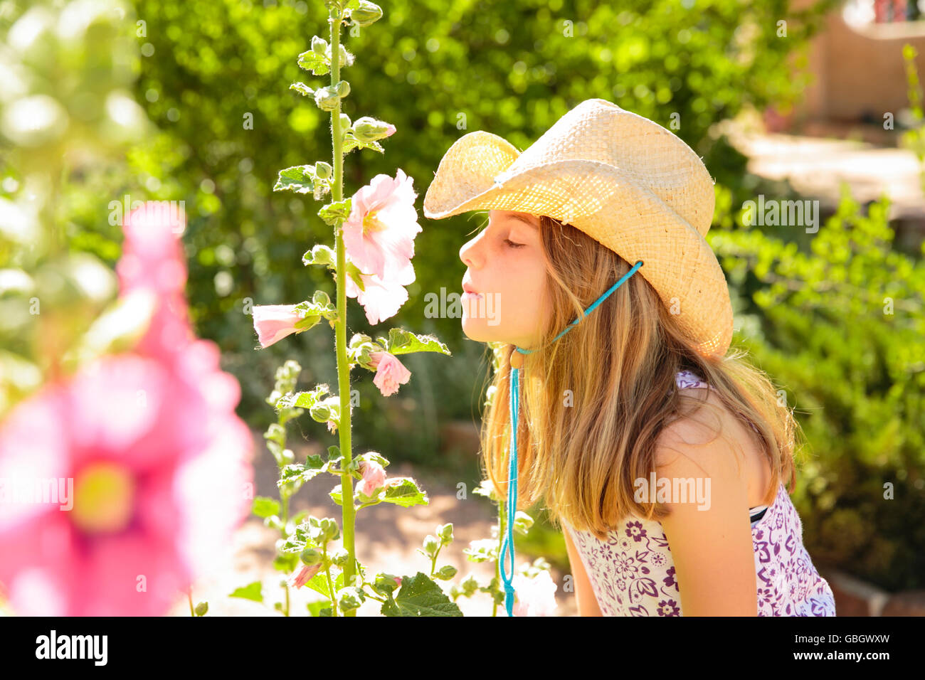 Young girl wearing cowboy hat smells a flower Stock Photo