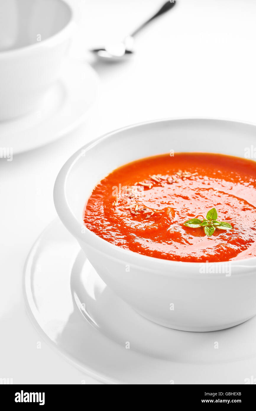 Picture of a white bowl with tomato cream soup with basil leaves on top, shallow depth of field. Stock Photo