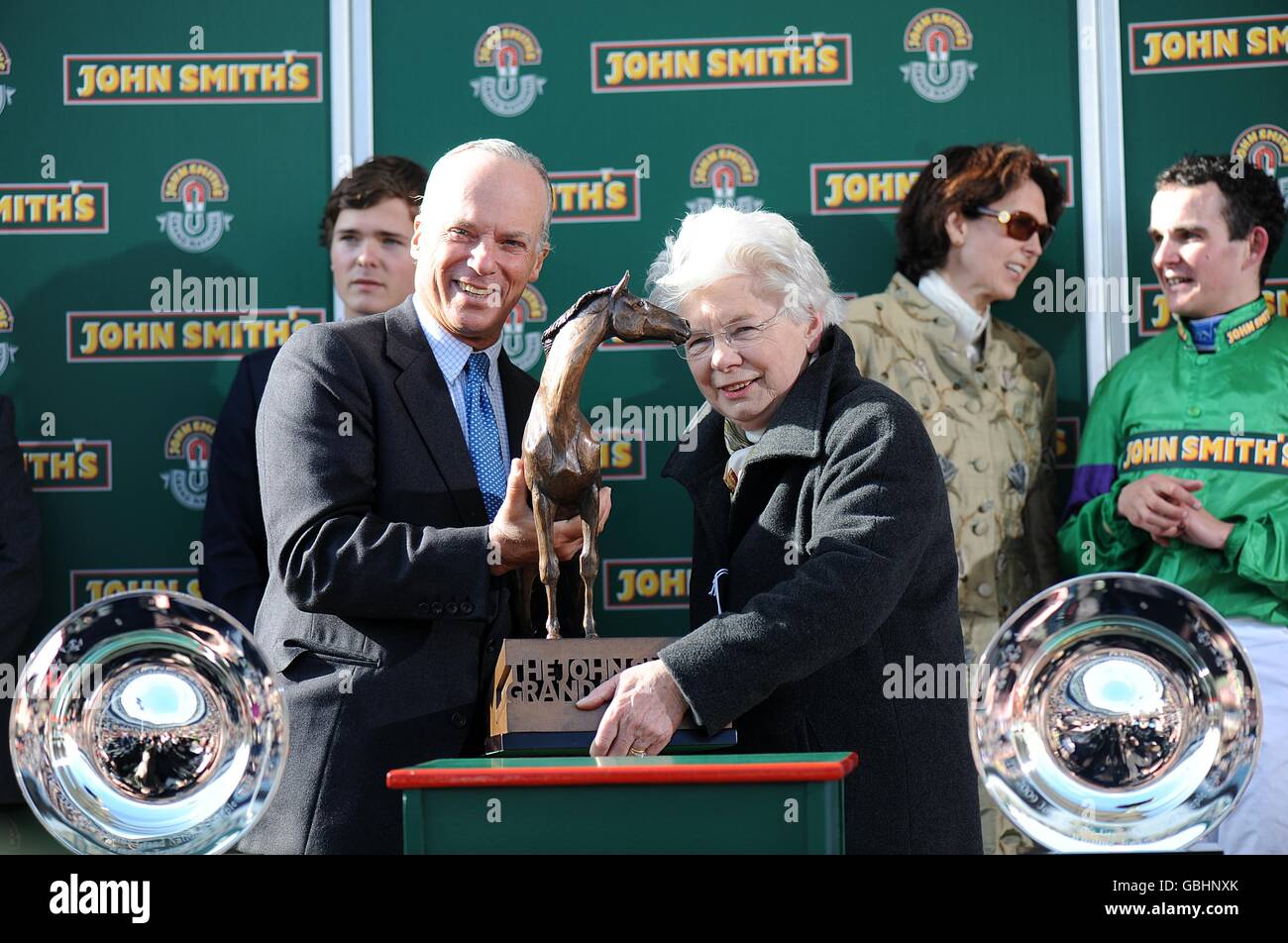 Owner Mrs Vida Bingham (right) is presented with the trophy for Mon Mome's victory in the John Smith's Grand National as trainer Venetia Williams and jockey Liam Treadwell chat in the background Stock Photo