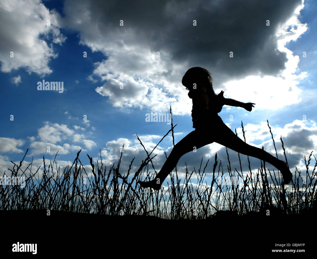 Silhouette of a child running and jumping in long grass Stock Photo