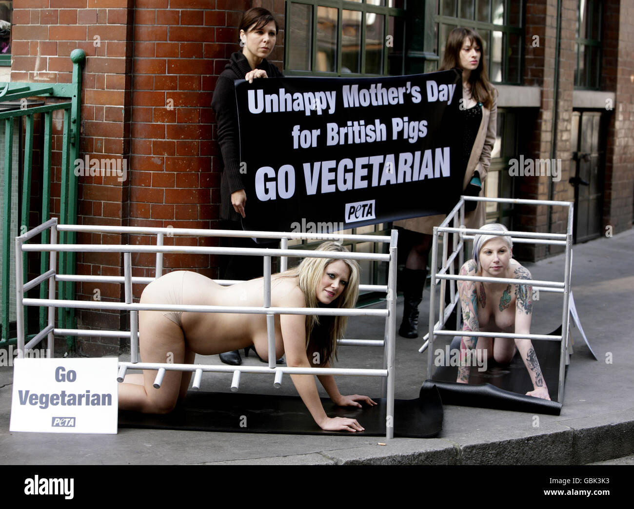 A banner reads 'Unhappy Mother's Day for British Pigs' during a PETA demonstration which featured two heavily pregnant PETA members, Hollie, 9 months pregnant, right, and Linzi, 6 months pregnant. Both women were in enclosures similar, in size, to the space that sows are typically confined to for a month while they are pregnant. Outside Jamie Oliver's Fitfteen restaurant in east London. Stock Photo