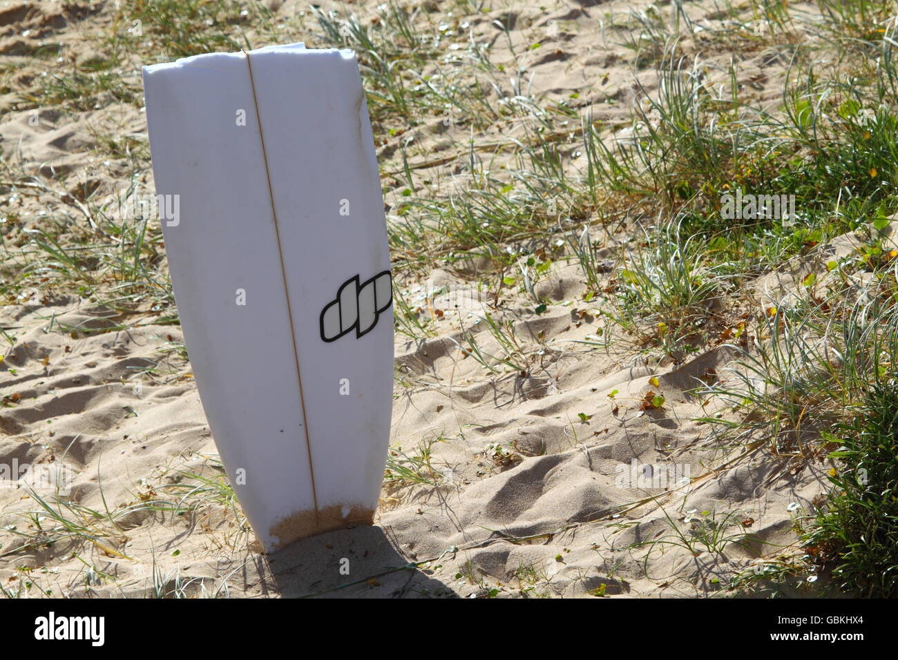 A section of a broken surfboard stuck into the beach sand after