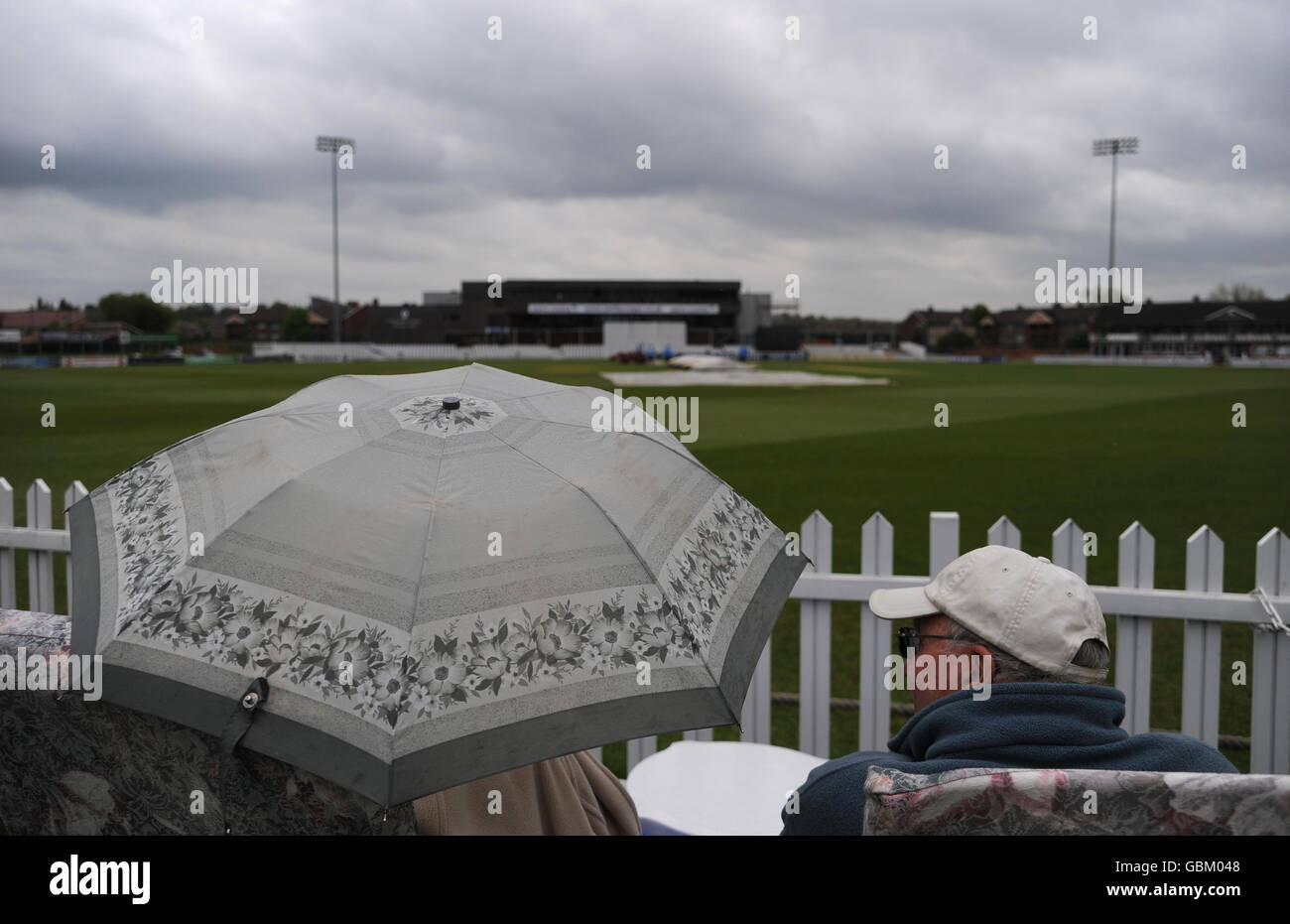 Spectators shelter under umbrellas as the rain forces the covers on after only a few overs of play during the Tour Match at the County Ground, Derby. Thursday April 30, 2009. See PA story CRICKET England Lions. Photo credit should read: PA Wire. Stock Photo