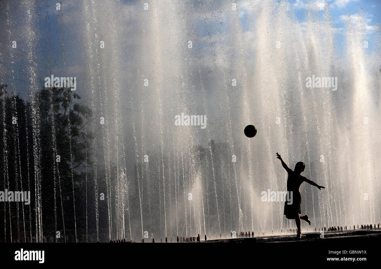 A child throws a ball as he cools off in fountains during hot weather in Almaty, Kazakhstan. Stock Photo