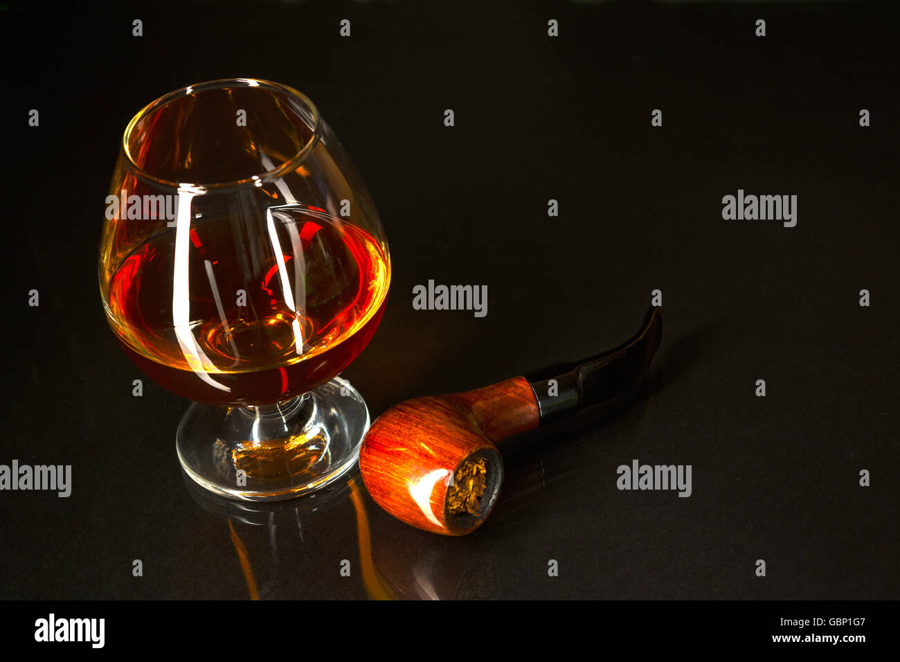 Whiskey glass and smoking pipe on black background. Cognac glass