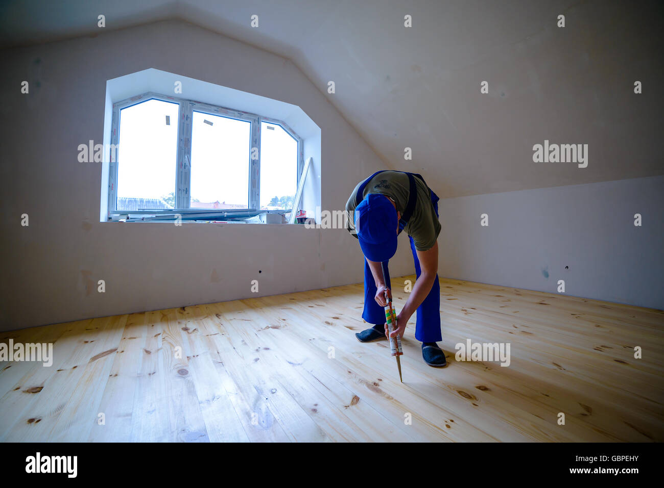 Wooden floor varnished. Worker with silicon gun. Stock Photo
