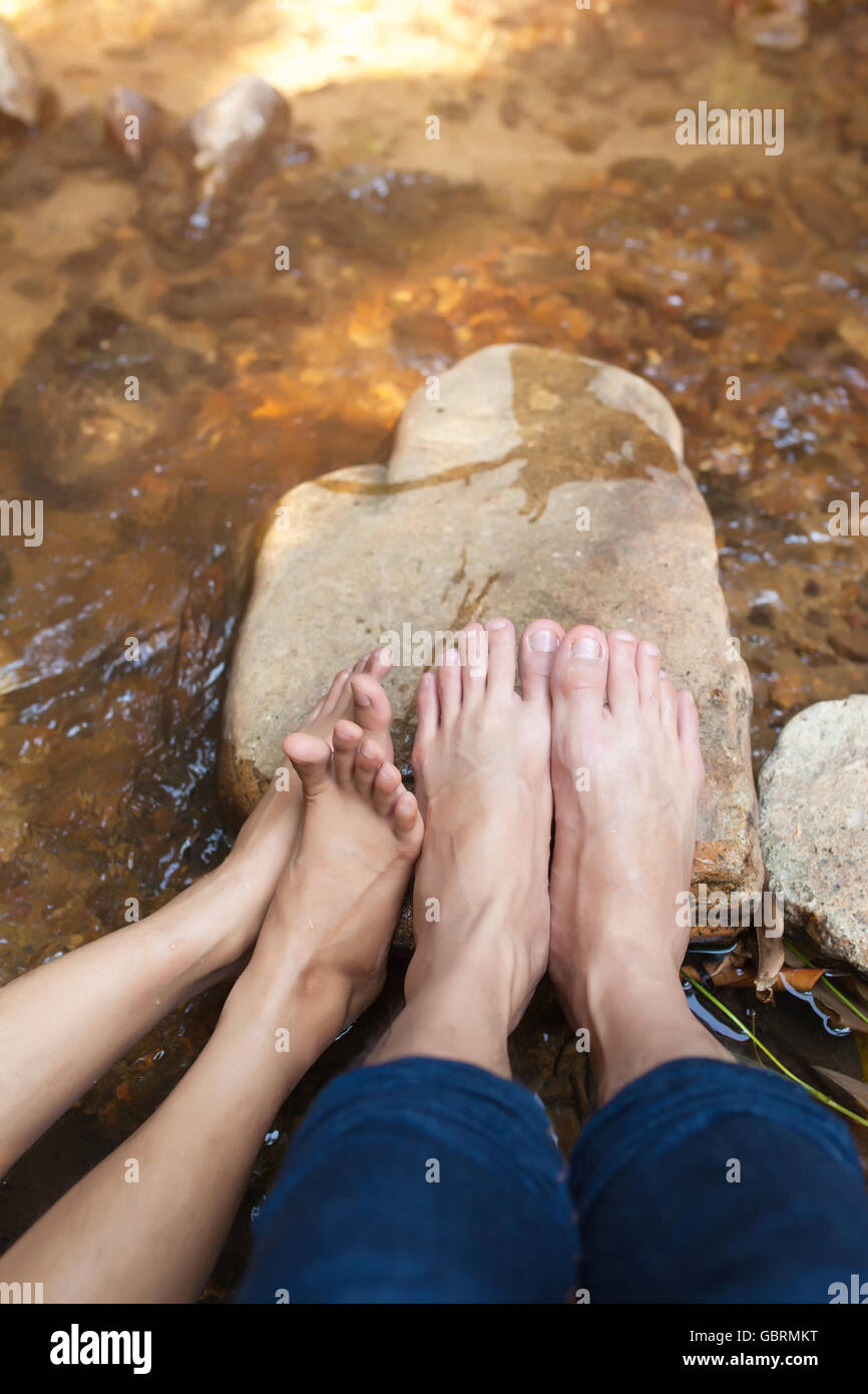 Feet of couple sitting on the stone near river. Stock Photo