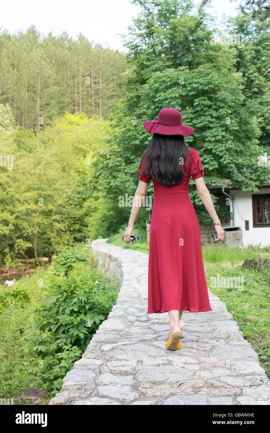 Woman walking the path in park wearing red dress Stock Photo