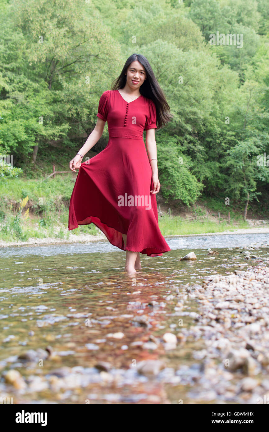 Fashionable woman walking in a river alone wearing red dress Stock Photo