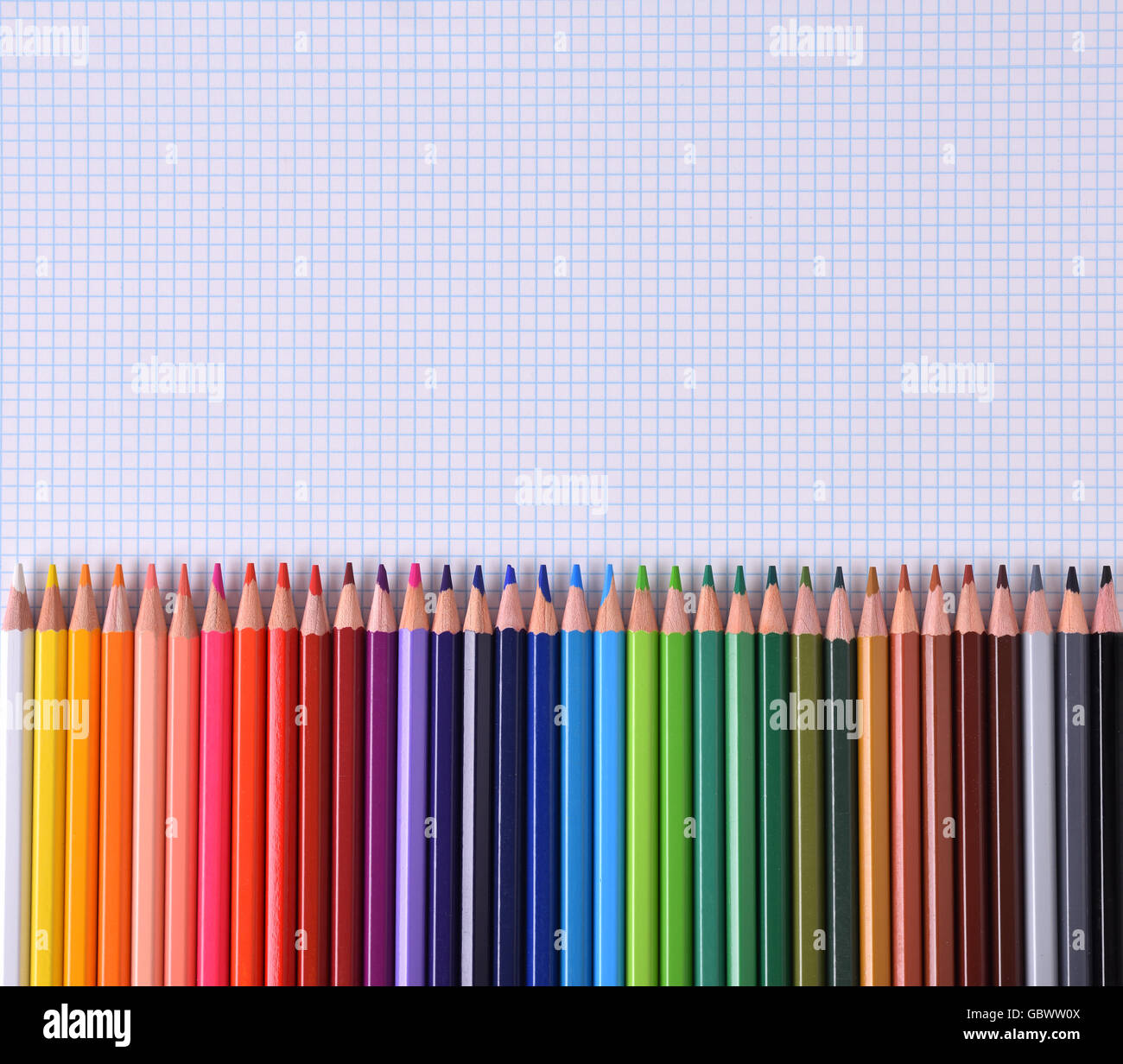 Colored pencils lined up palette on checkered white sheet of paper. Top