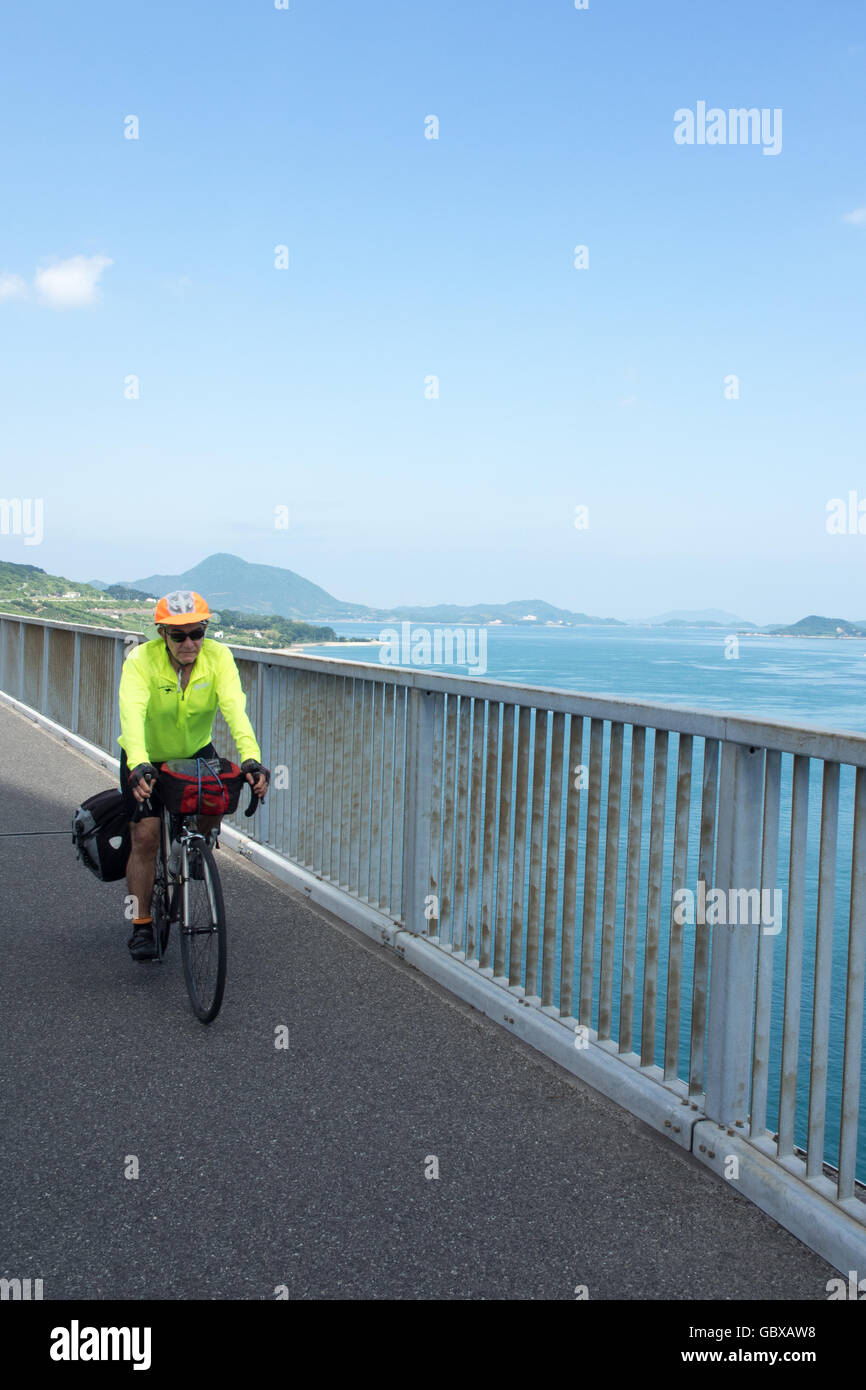 A touring cyclist cycling across the Tatara Bridge connecting the islands of Omishima and Ikuchi in the Seto Inland Sea. Stock Photo