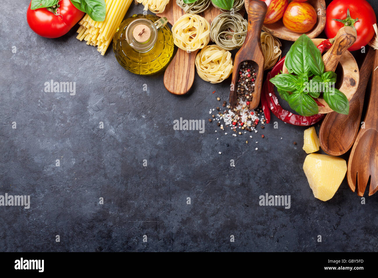 Italian food cooking. Tomatoes, basil, spaghetti pasta, olive oil and chili pepper on stone kitchen table. Top view with copy sp Stock Photo