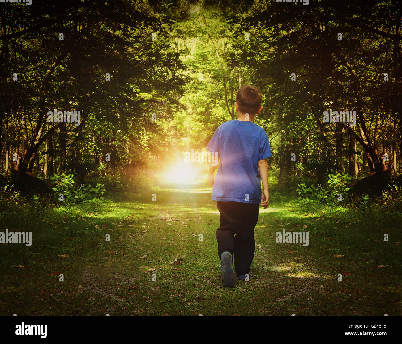 A child is walking in the dark woods into a bright light on a path for a freedom or happiness concept. Stock Photo