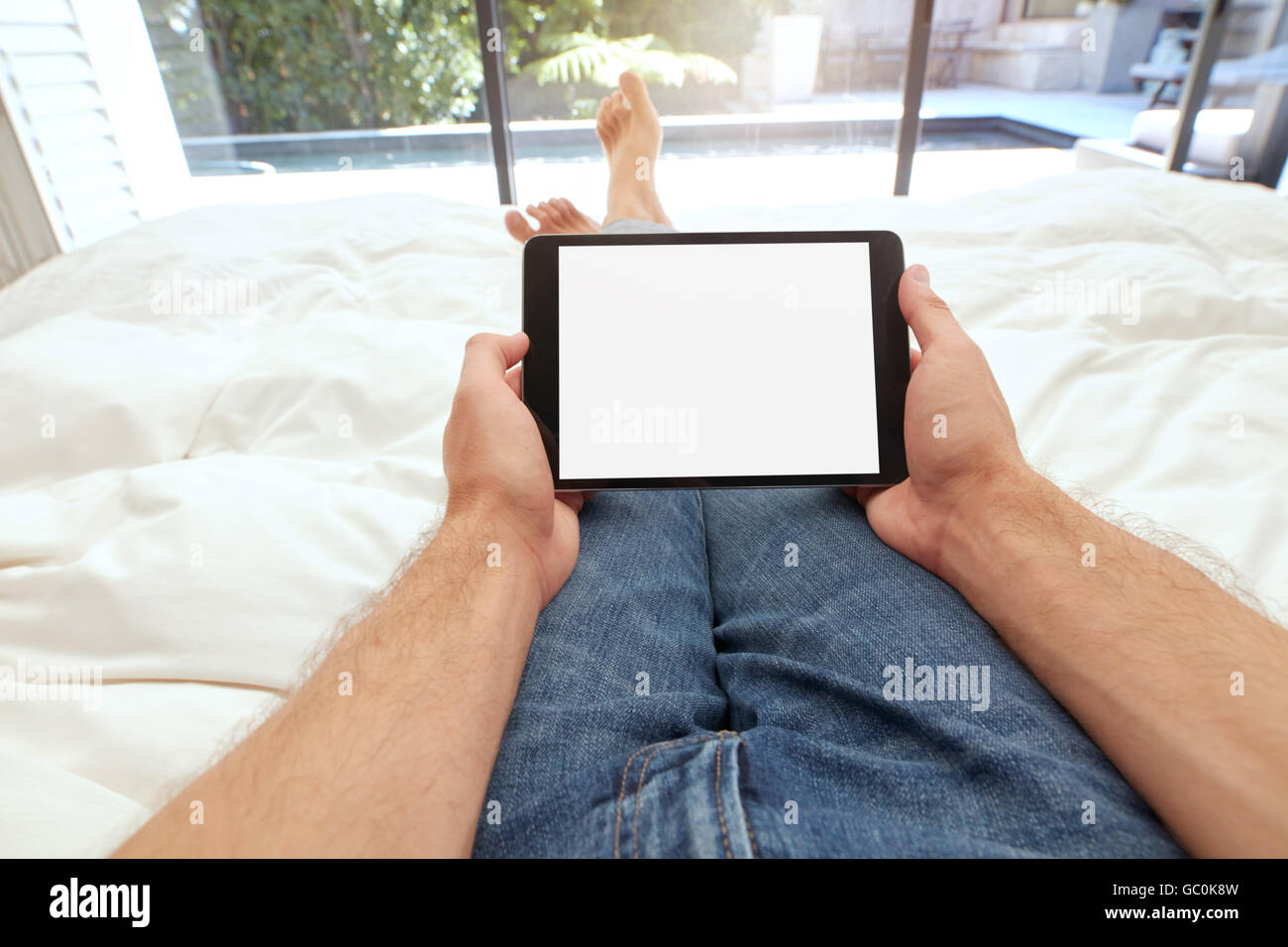 Closeup image of man holding a blank touch screen computer on bed. POV shot of man lying on bed using digital tablet. Stock Photo