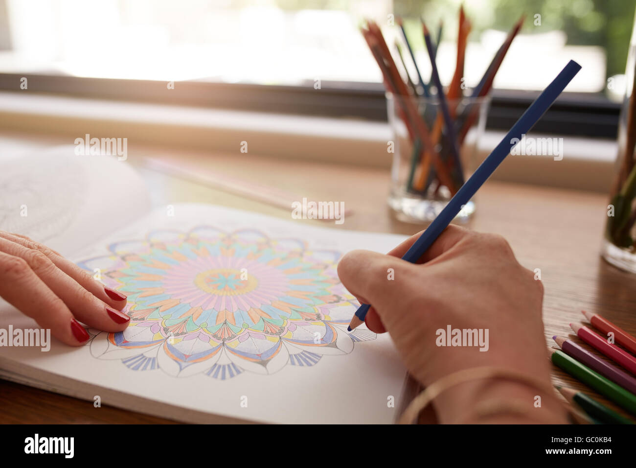 Close up of human hands drawing in adult coloring book with colored pencil at home. Relieving stress with pencil coloring in boo Stock Photo