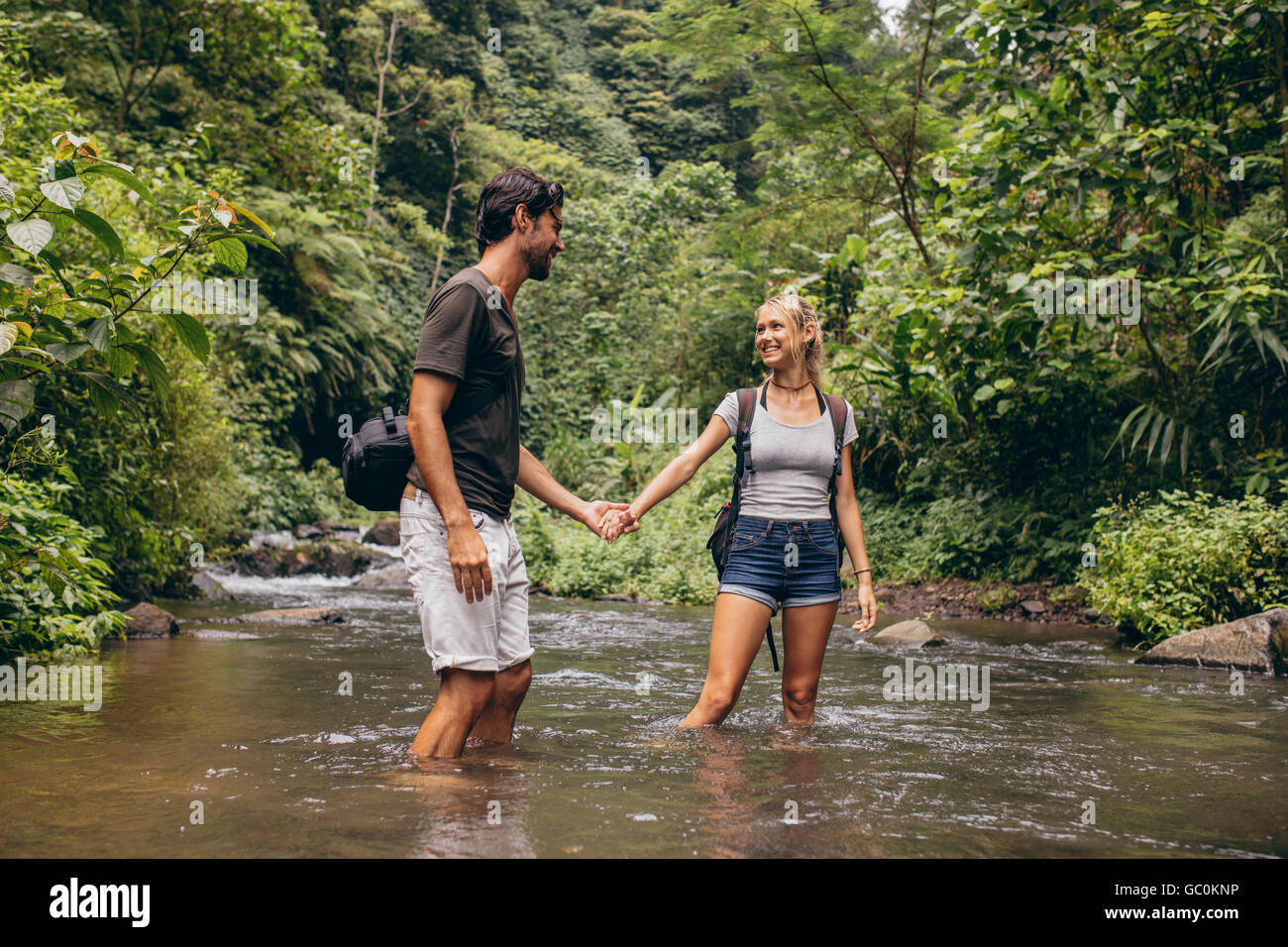 Loving young couple standing in forest stream. Young man and woman standing in river holding hands. Having fun on hiking day. Stock Photo