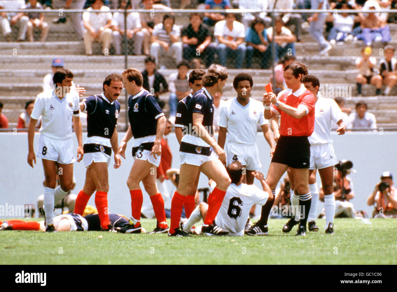 Referee Joel Quiniou (second r) shows the red card to Uruguay's Jose Batista (6, on floor) after he hacked down Scotland's Gordon Strachan (l, on floor) in the first minute of the game. Milling around are Scotland's Willie Miller (second l), Steve Nicol (third l), Paul McStay (fourth l) and Roy Aitken (fifth l), and Uruguay's Jorge Barrios (l) and Victor Diogo (third r) Stock Photo