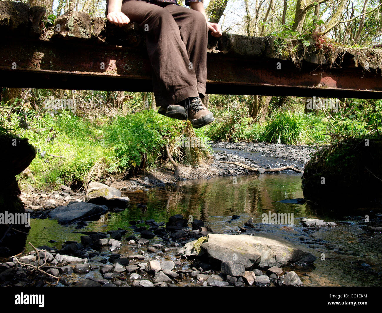 Walker sat on rustic bridge over stream, Devon, UK Stock Photo