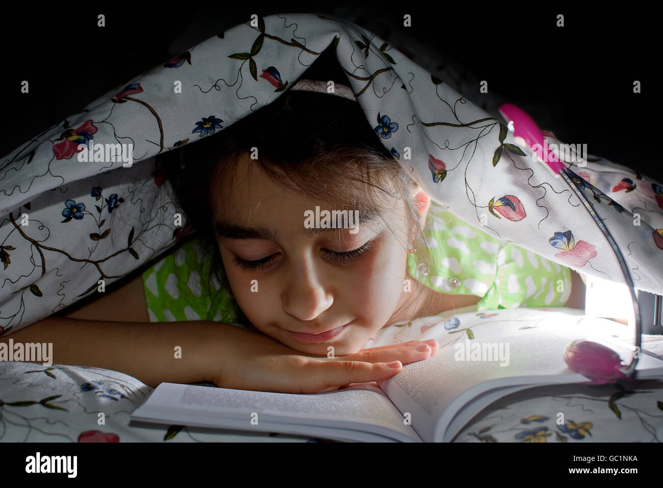 little girl reading a book in bed Stock Photo