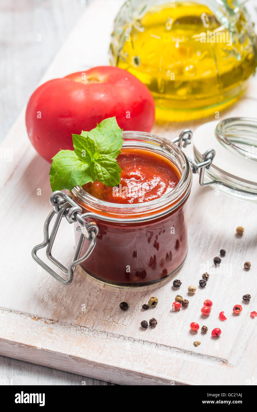 Glass jar with homemade classic spicy tomato pasta or pizza sauce. Italian healthy food on white wooden background. Stock Photo