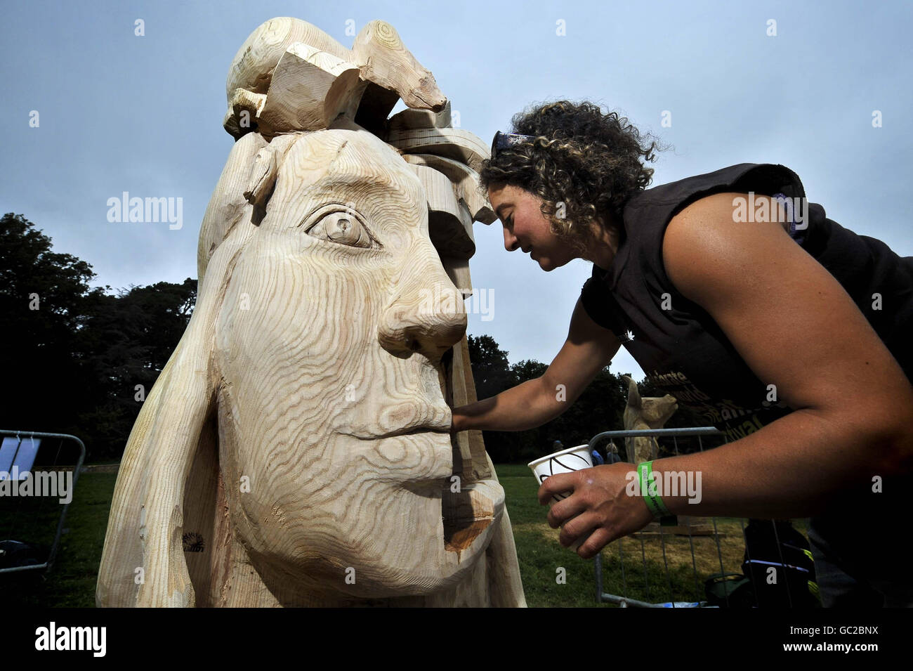 Freelance chainsaw carver Mandy Schmidt begins the finishing touches as she brushes Norwegian oil onto her wood sculpture of the fictional character 'Medusa' at the Festival of the Tree, Westonbirt Abouretum, Gloucestershire. Stock Photo