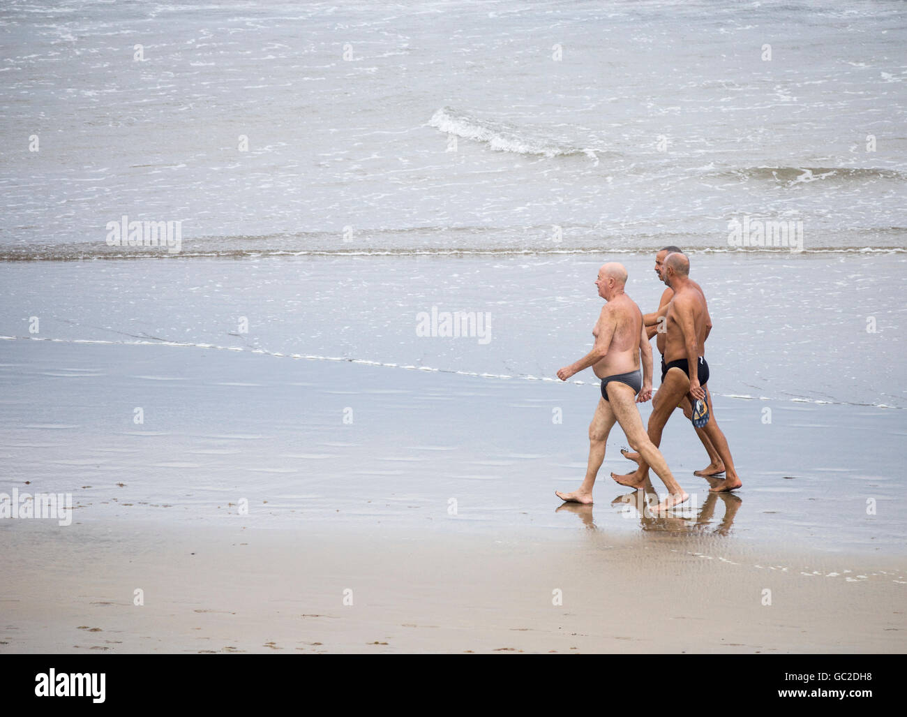 Three elderly men walking on beach in Spain Stock Photo