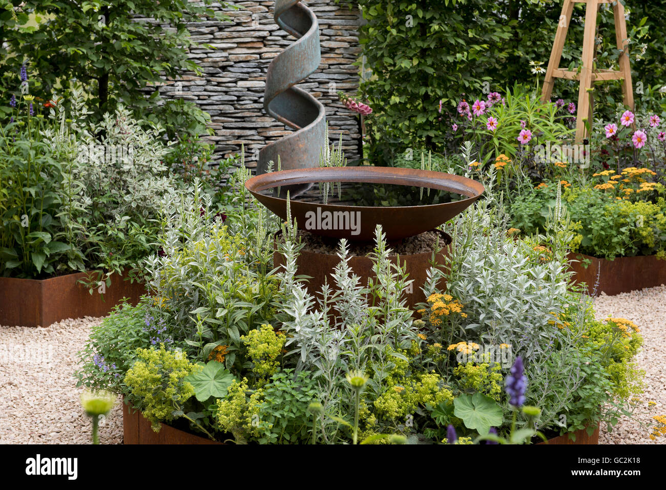 Naturalistic planting around a metal water feature in the A Summer Retreat Garden at The Hampton Court Palace Flower Show 2016, Stock Photo
