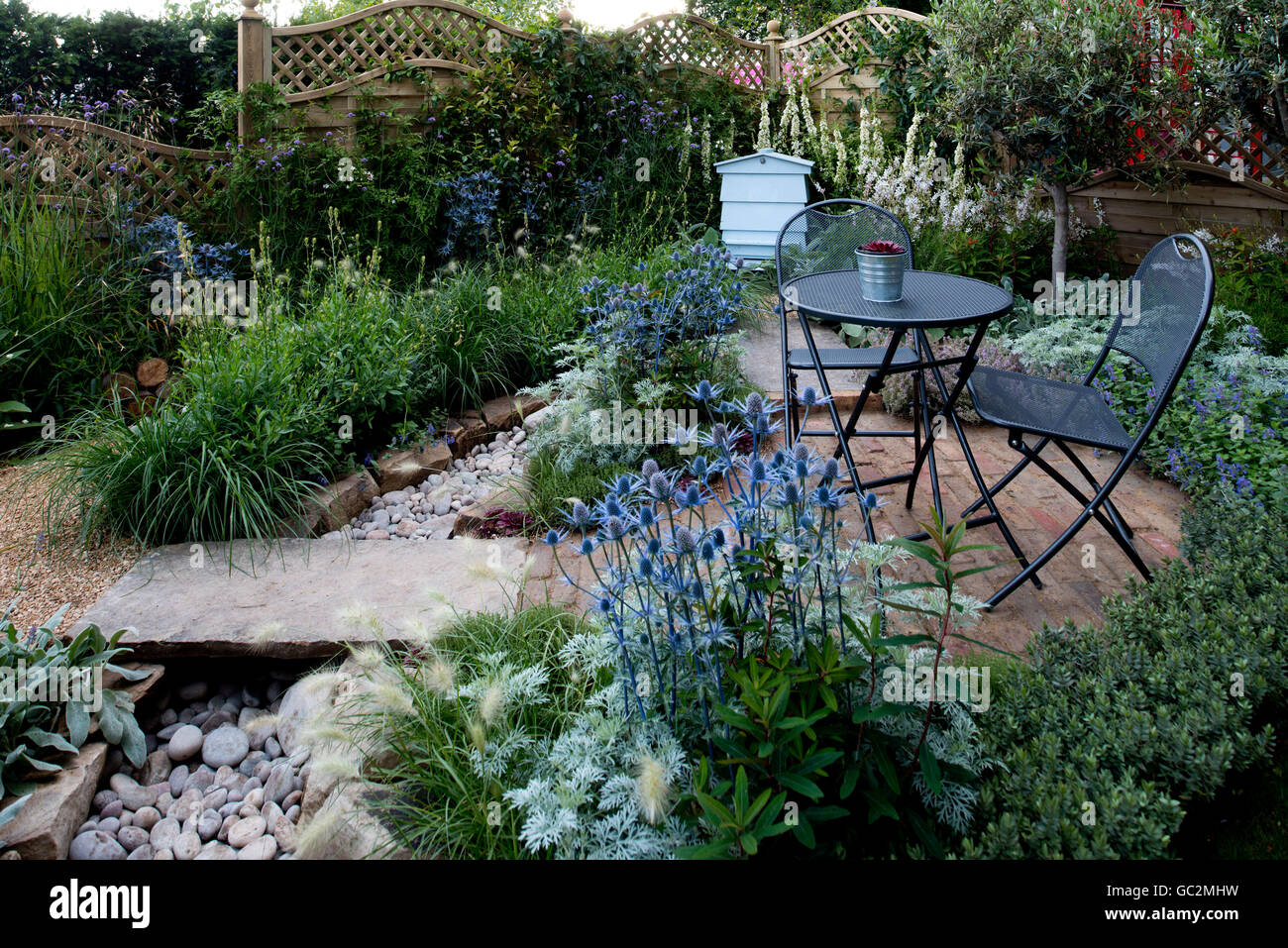 A metal table and chairs and a beehive  surrounded by plants in the Drought Garden at the Hampton Court Palace Flower Show 2016 Stock Photo