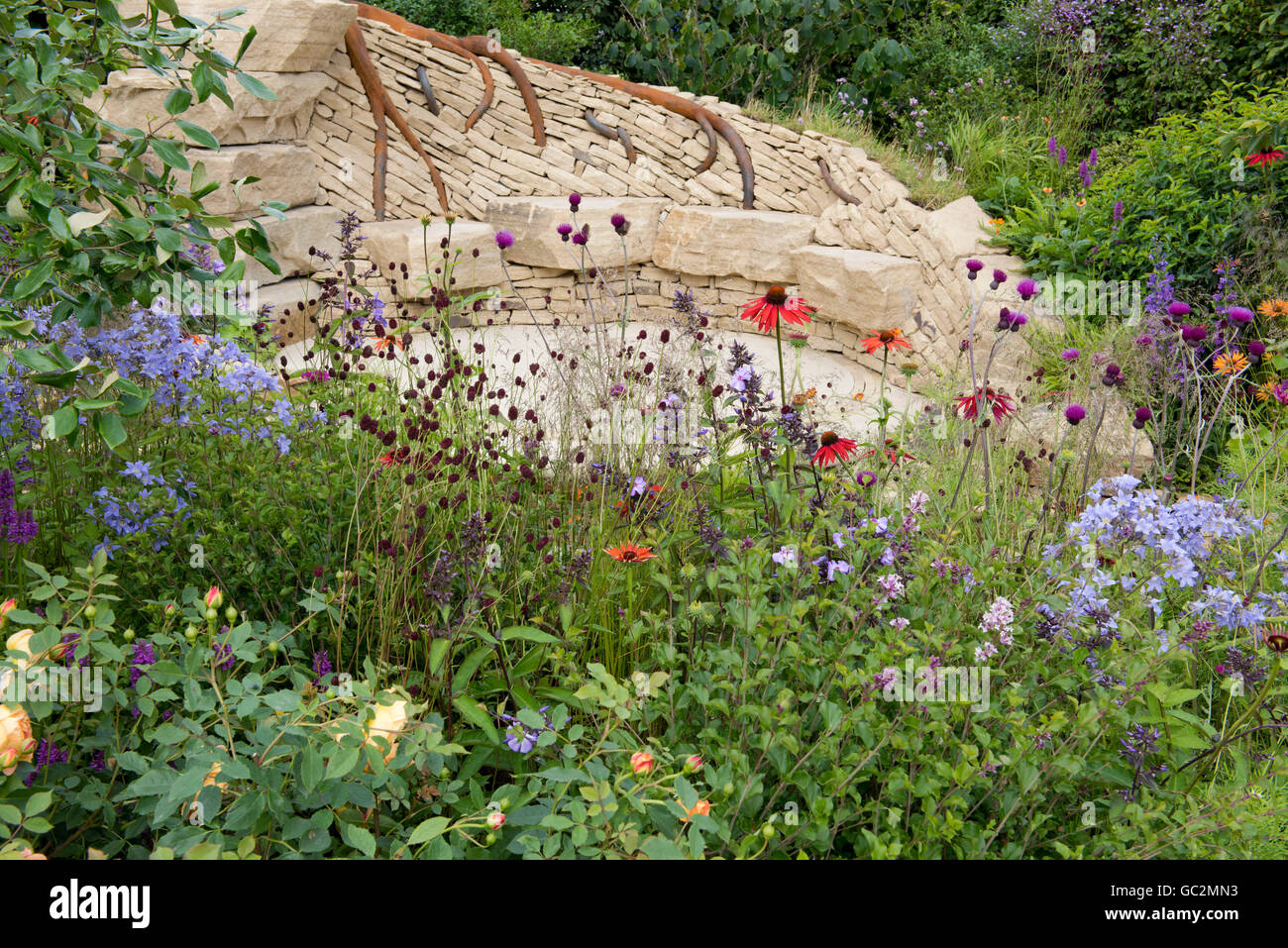 A stone seating area surrounded by naturalistic planting in The Zooflora: Outstanding Natural Beauty Garden. Stock Photo