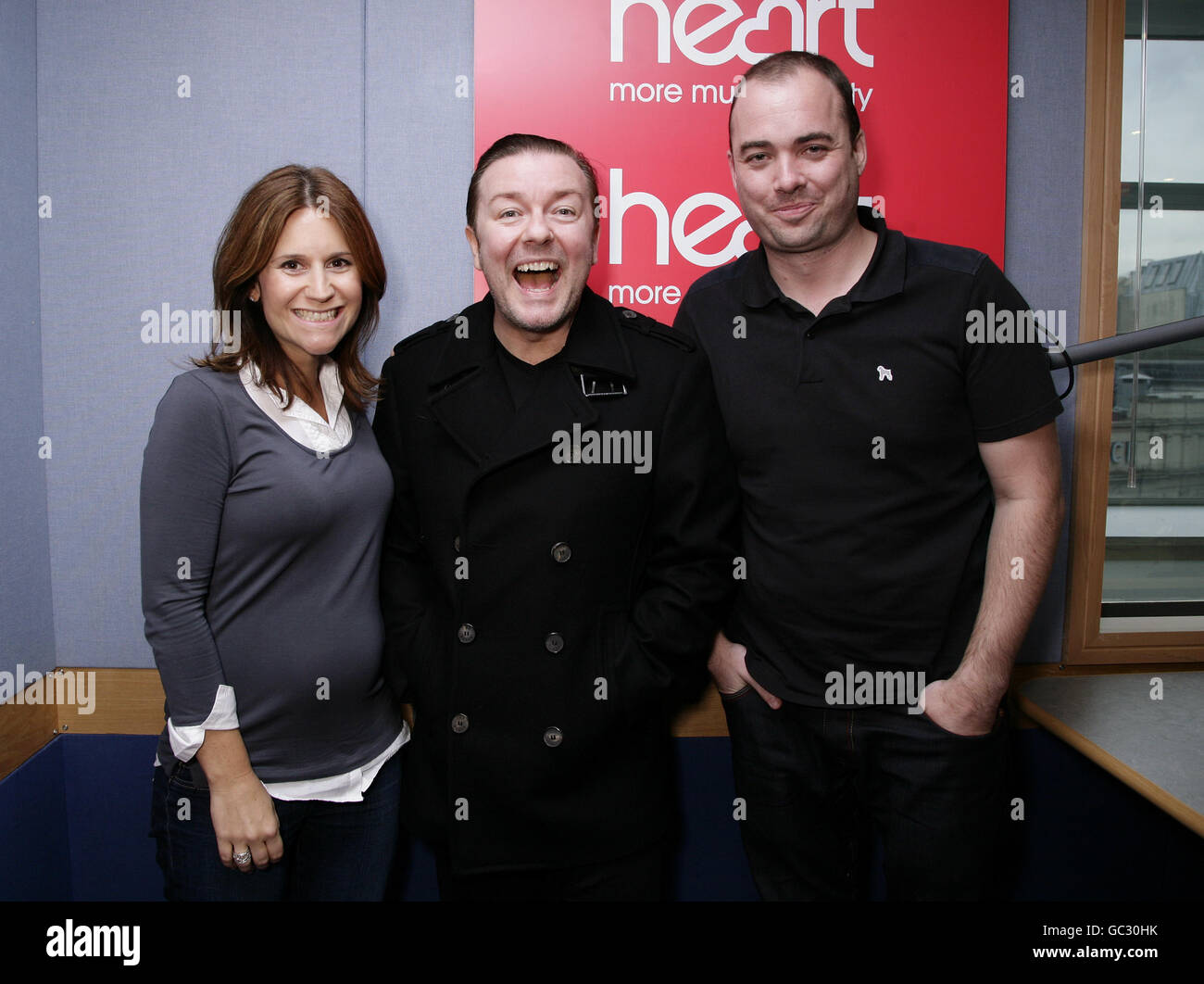 Guest Ricky Gervais (centre) with Heart show presenters Harriet Scott and Neil Bentley at Global Radio in Leicester Square, central London. Stock Photo