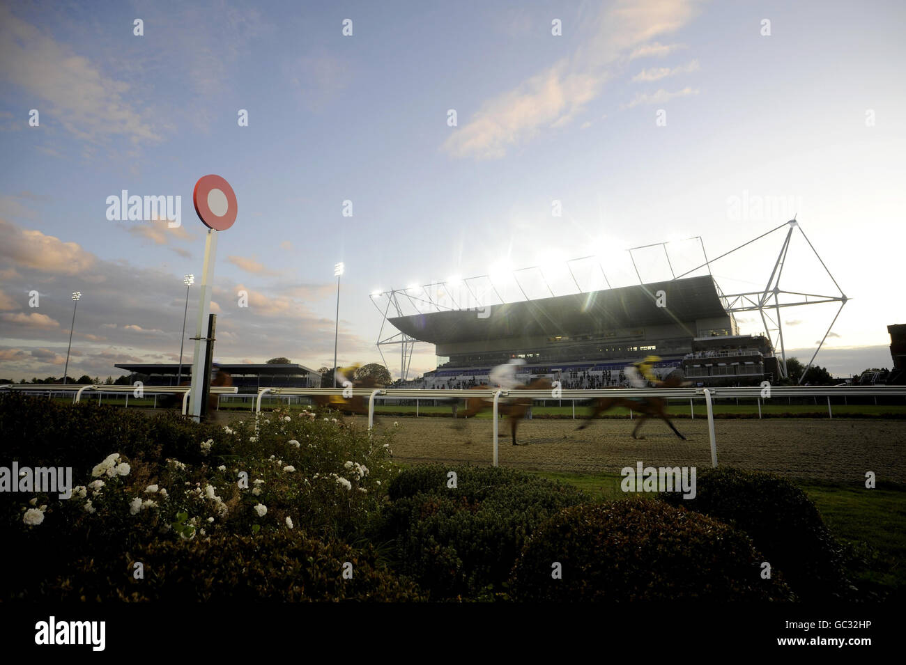Runners and riders pass the winning post and grandstand in the Midland Facilities Management E.B.F. Maiden Fillies' Stakes at Kempton Park Racecourse. Stock Photo