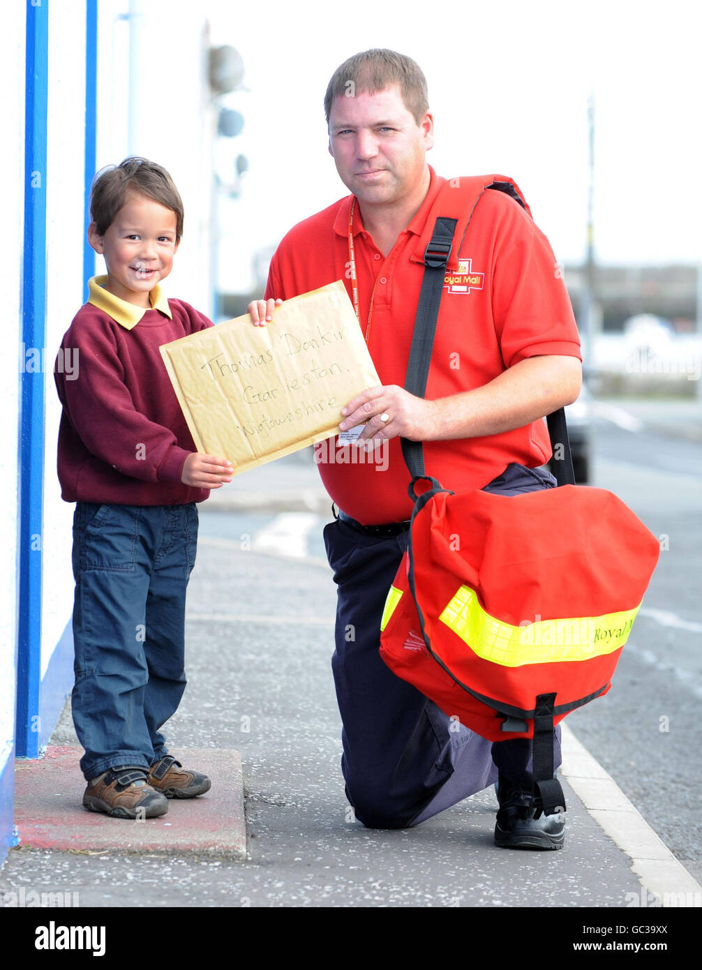 Four-year-old Thomas Donkin from Garlieston, Wigtownshire in Scotland, receives his new book from the Dolly Parton Imagination Library, the 100,000th book to be delivered through its UK programme, from postman Alan McColm. Stock Photo