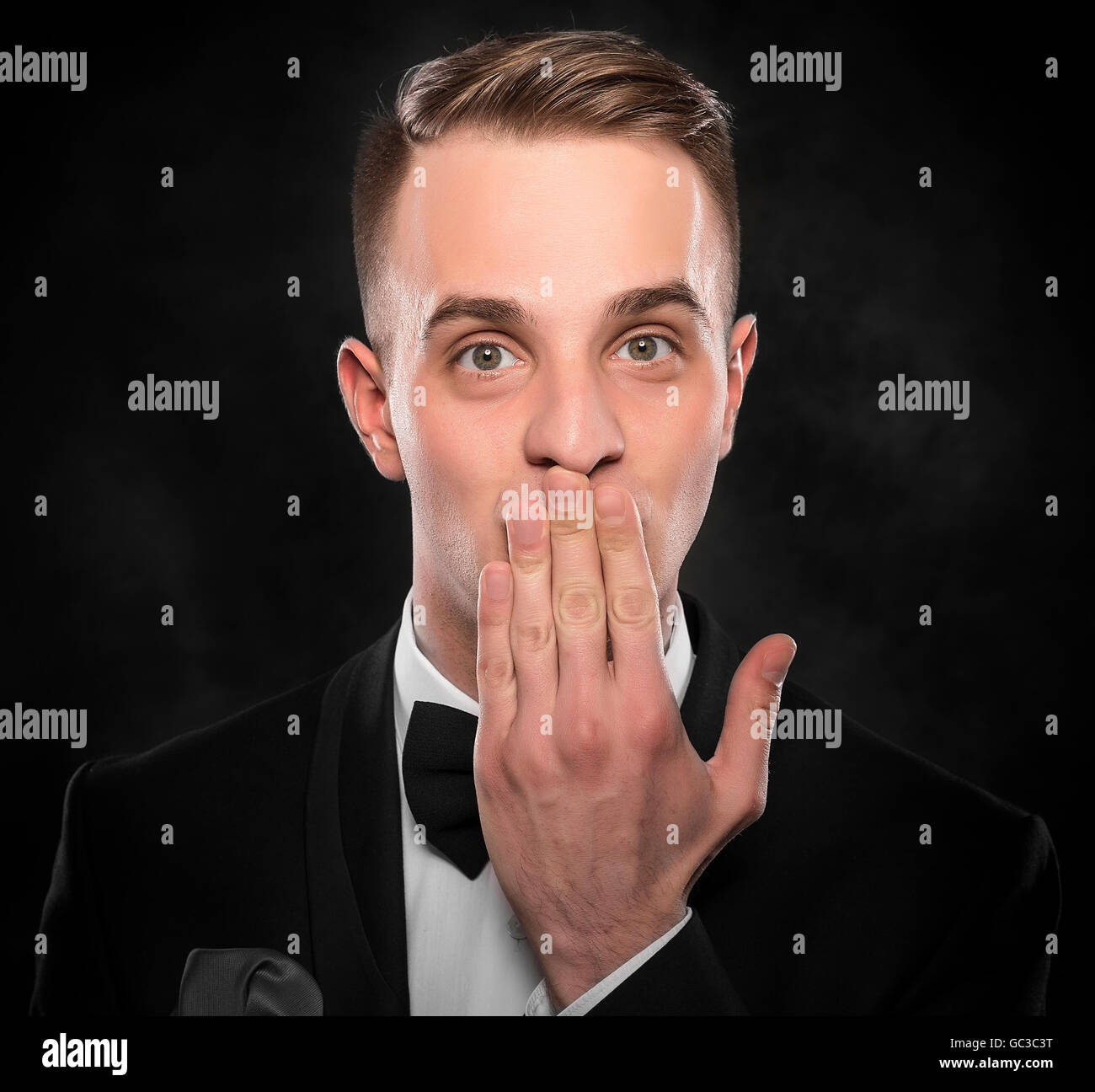Scared man in suit hand covering mouth over dark background. Stock Photo