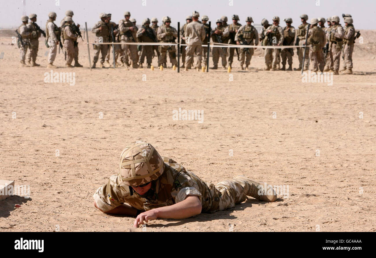 A British Army Soldier on a training exercise looking for improvised explosive devices (IEDs) at Camp Bastion in Afghanistan with American Marines in the distance. Stock Photo