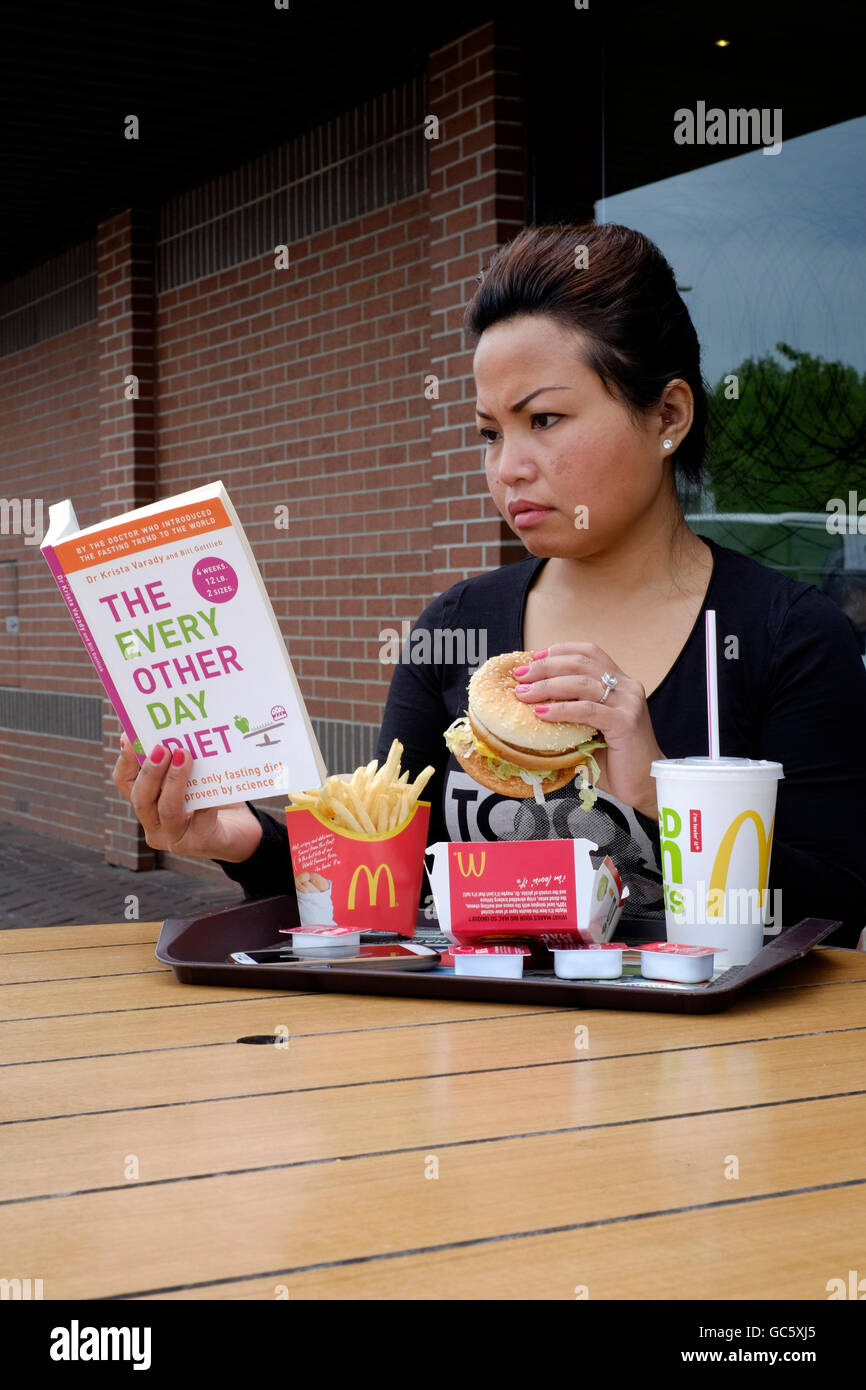 Reading Eating young female reading dieting book while eating a large burger in ...