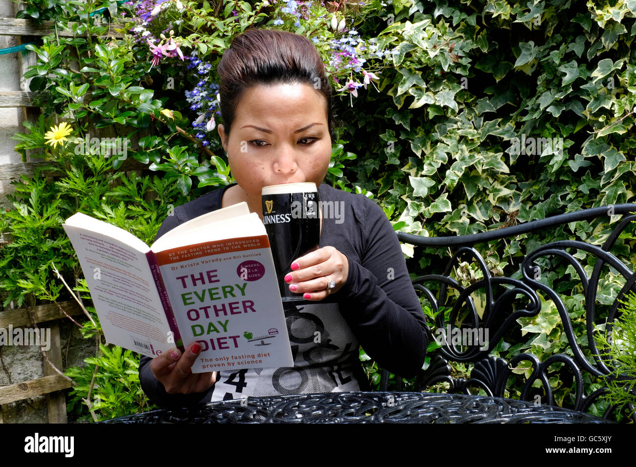 young female reading dieting book while drinking beer in a pub garden in england uk Stock Photo