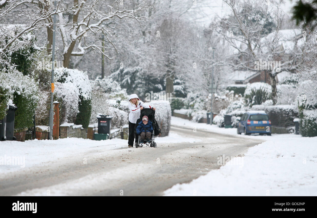A woman struggles to push her buggy along an ungritted road in Knutsford, Cheshire. Stock Photo