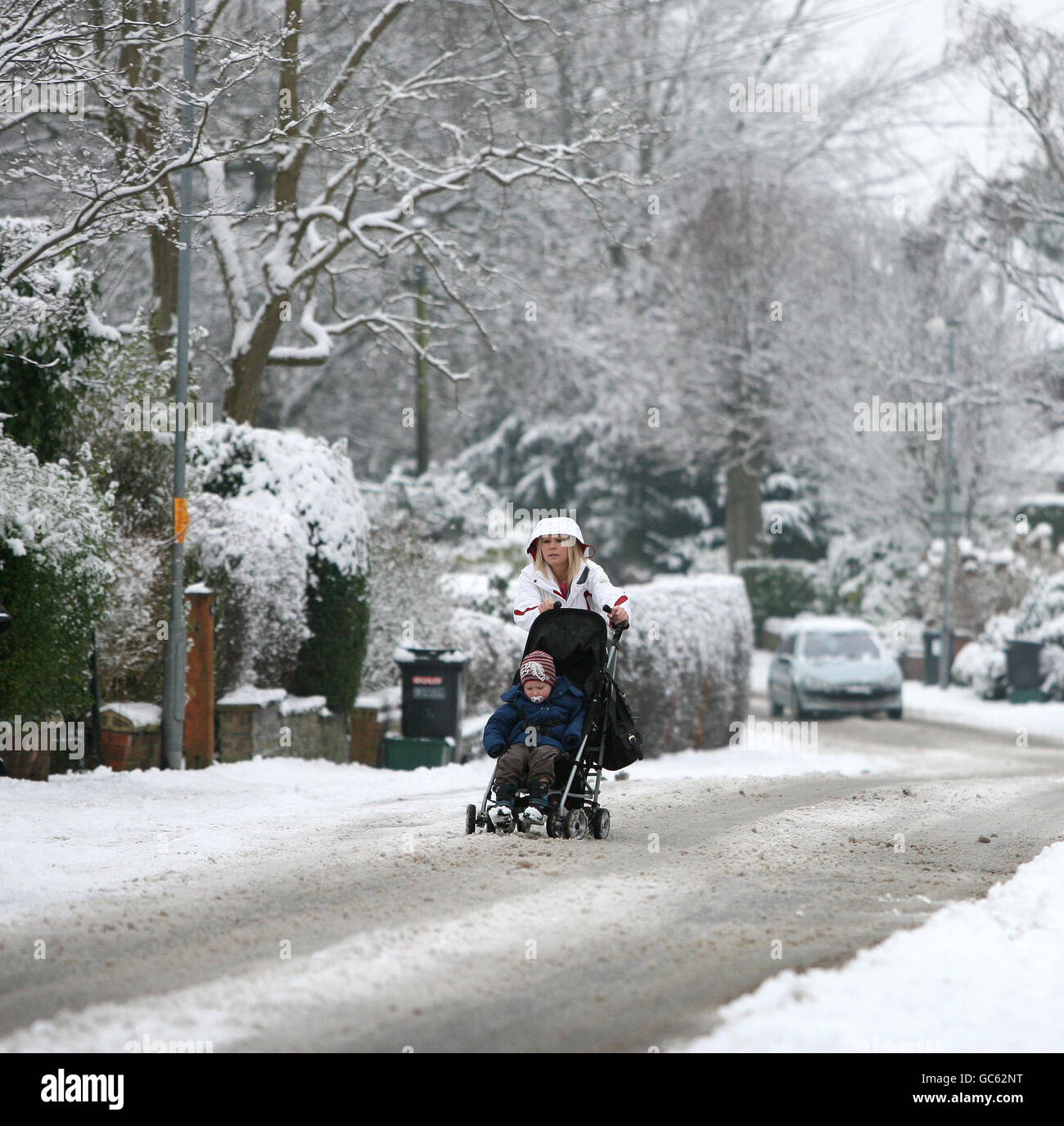 A woman struggles to push her buggy along an ungritted road in Knutsford, Cheshire. Stock Photo