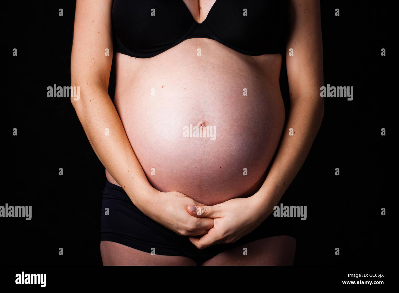 Pregnancy belly with her hands under the belly. Dark tone. Stock Photo