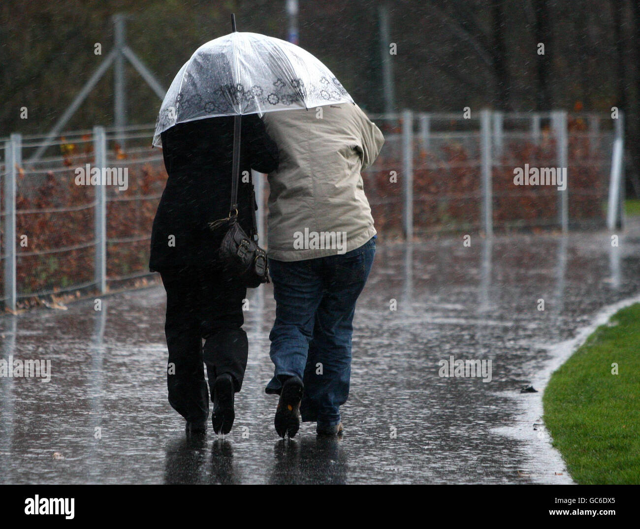 Two people shelter under the same umbrella in the rain and wind outside