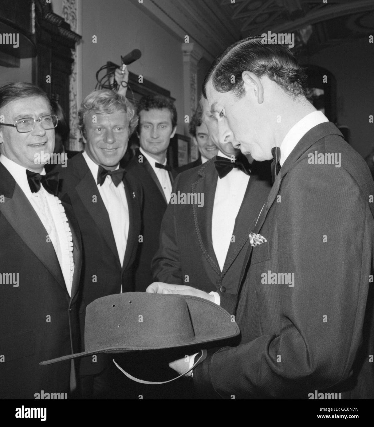 The Prince of Wales looks at a 'bush hat' at the Classic Cinema in Haymarket, London, when he attended the Royal Gala Charity Premiere of the film 'Breaker Morant'. Looking on are two of the stars, Edward Woodward, left, and Australian actor Jack Thompson. Stock Photo