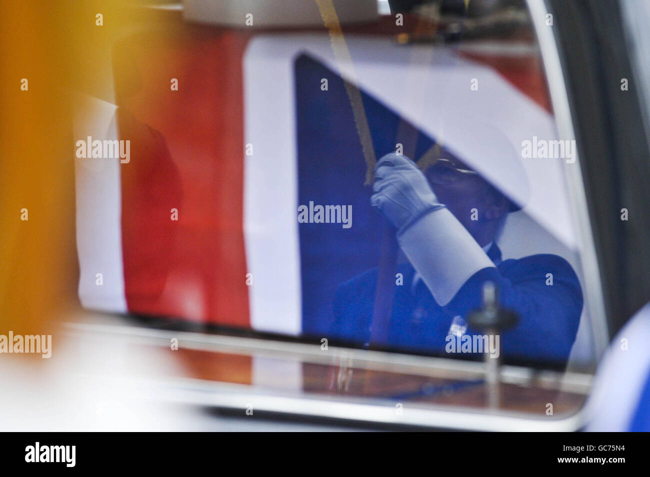 A standard bearer is reflected in the hearse window at the funeral of