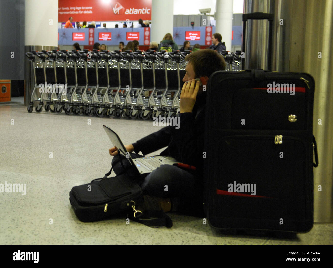 A stranded passenger at Gatwick Airport uses a phone and laptop waiting ...